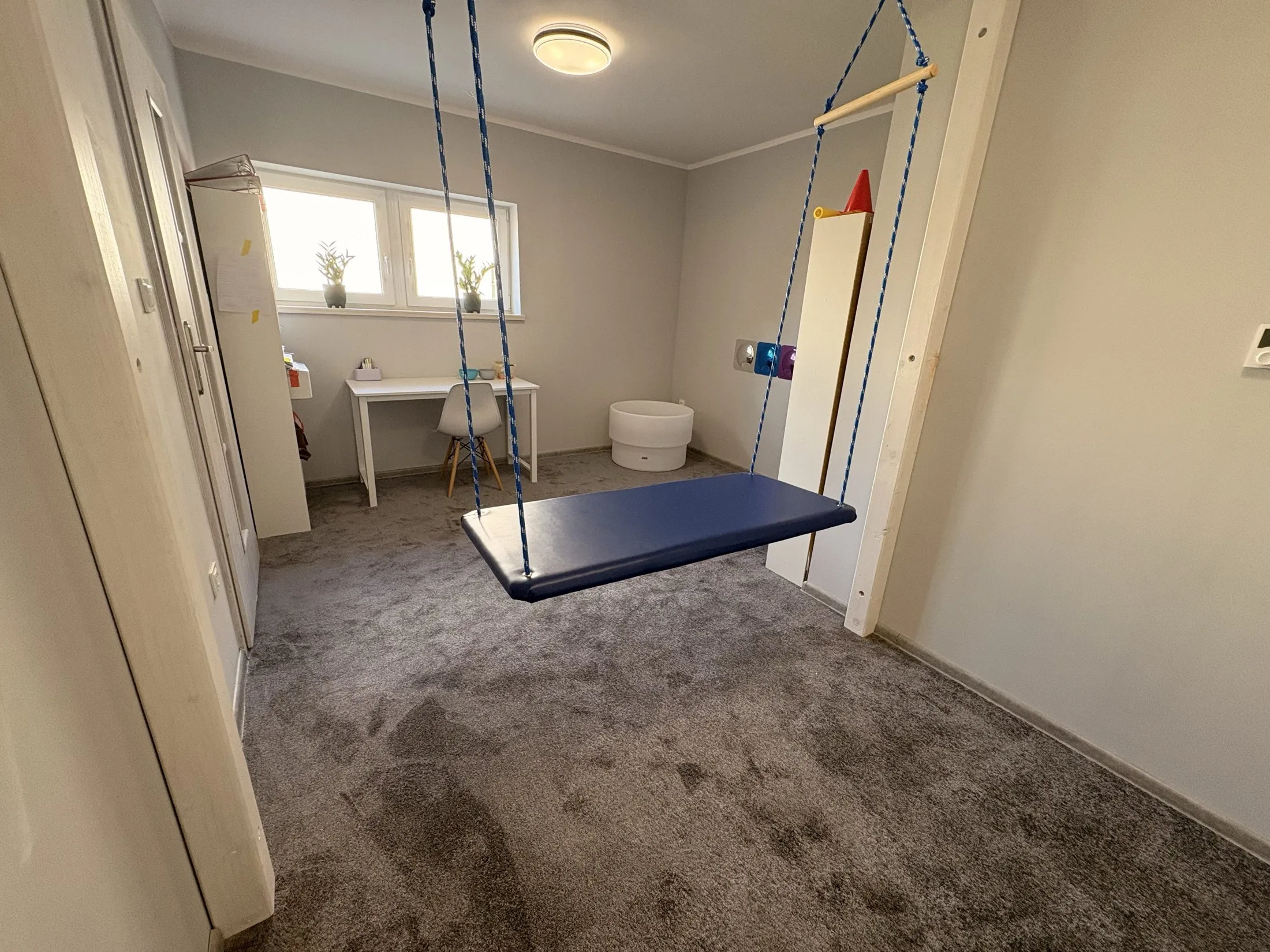 Sala terapii integracji sensorycznej w Redzie: huśtawka platformowa, stolik do pracy i okno